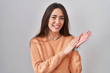 Genç esmer kadın beyaz arka planda ayakta alkışlıyor ve mutlu ve neşeli alkışlıyor, gururla gülümsüyor. 