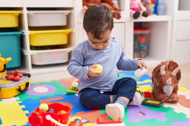 Anaokulunda yerde oturmuş süpermarket oyunu oynayan sevimli İspanyol çocuk.