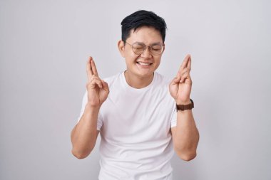 Beyaz arka planda duran Asyalı genç adam umut ve gözlerin kapalı gülümseyerek el sallıyor. Şans ve batıl inançlar. 