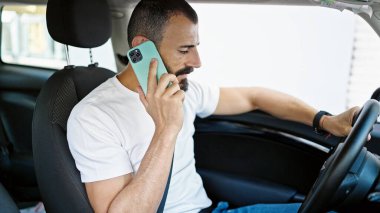 Genç İspanyol adam akıllı telefondan konuşuyor. Sokakta arabada oturuyor.