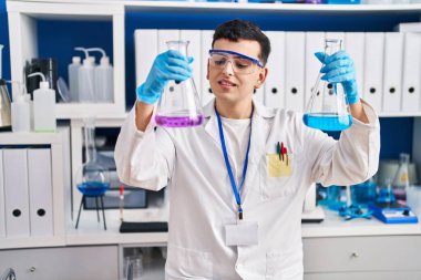 Young non binary man scientist smiling confident measuring liquid at laboratory
