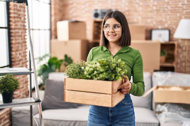 Genç, güzel, İspanyol bir kadın gülümsüyor. Yeni evinde tahta saksı tutuyor.