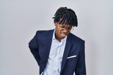 Rasta giyen Afrikalı genç bir adam beyaz arka planda iş ceketi giyiyor sırt ağrısı çekiyor, elle dokunuyor, kas ağrısı çekiyor. 