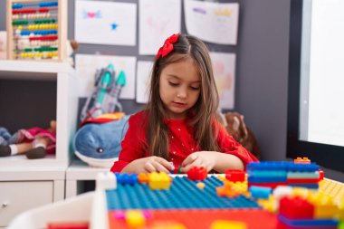 Anaokulundaki masada oturan, inşaat bloklarıyla oynayan sevimli İspanyol kız.