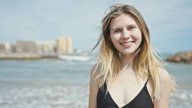 Kumsalda gülümseyen bikinili genç sarışın kadın turist.