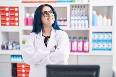 Young caucasian woman pharmacist smiling confident standing with arms crossed gesture at pharmacy