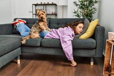 Genç, güzel, İspanyol bir kadın kanepede uzanıyor ve evde köpekle yatıyor.