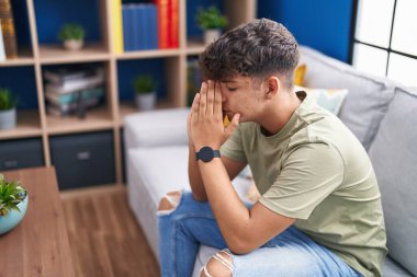 Young hispanic teenager stressed sitting on sofa at home