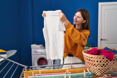 Gömleğini tutan genç sarışın kadın çamaşırhanede çamaşır ipine asıyor.