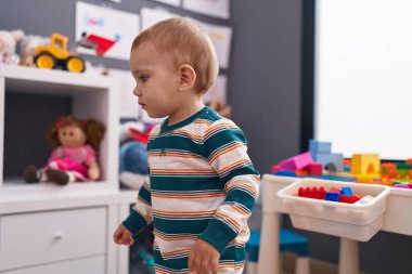 Anaokulunda rahat bir ifadeyle duran sevimli beyaz bebek.