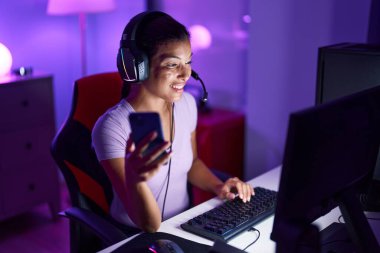 Oyun odasında bilgisayar ve akıllı telefon kullanan genç, İspanyol asıllı güzel bir kadın.