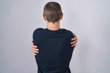 Beyaz, sarışın, bitcoin tişört giyen, kendine sarılan, mutlu ve pozitif bir adam. Sevgi ve özgüven. 