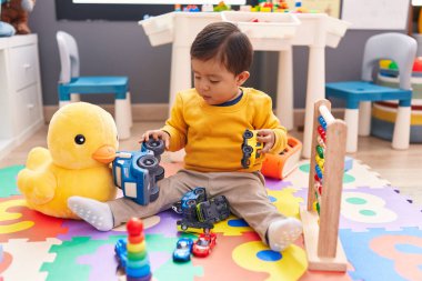 Anaokulunda yerde oturan sevimli İspanyol çocuk araba oyuncağıyla oynuyor.