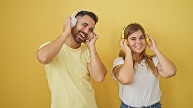 Kadın ve erkek, izole edilmiş sarı arka planda birlikte müzik dinliyorlar.