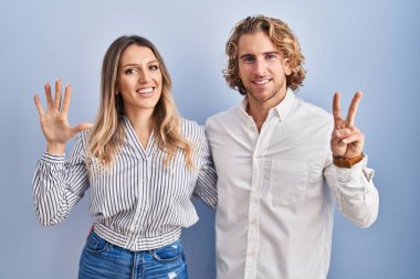 Mavi arka planda duran genç çift yedinci parmaklarını gösterip işaret ederken kendinden emin ve mutlu bir şekilde gülümsüyor.. 