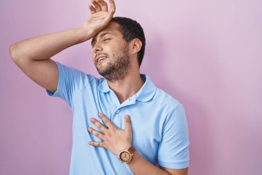 İspanyol adam pembe arka planda duruyor. Hastalık, ateş, grip ve virüs için alnına dokunuyor. 