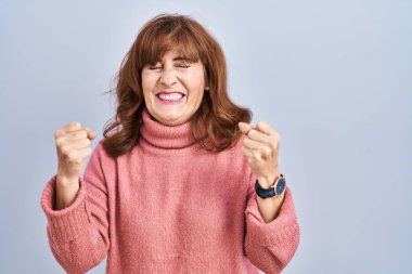 Orta yaşlı İspanyol bir kadın izole edilmiş arka planda duruyor. Kolları havada ve gözleri kapalı zaferi kutlarken heyecanla bekliyor. Kazanan konsept. 