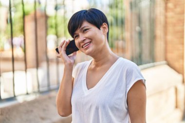 Orta yaşlı Çinli kadın gülümsüyor. Caddedeki akıllı telefondan kendine güvenen sesli mesaj dinliyor.
