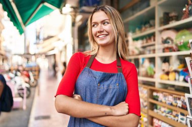 Young hispanic woman shop assistant standing with arms crossed gesture at street
