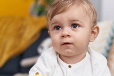 Evinde rahat bir ifadeyle kanepede oturan sevimli beyaz çocuk.