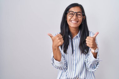 Genç İspanyol kadın gözlüklü başarı işareti takıyor. Elleriyle olumlu jest yapıyor. Gülümsüyor ve mutlu. Neşeli ifade ve kazanan jest. 