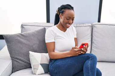 Evdeki koltukta oturan Afro-Amerikan kadın akıllı telefon kullanıyor