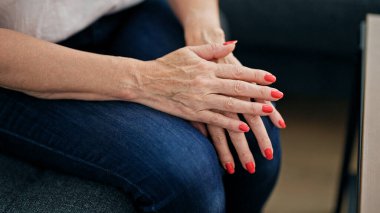 Orta yaşlı bir kadın kanepede oturuyor ve evde el ele tutuşuyor.