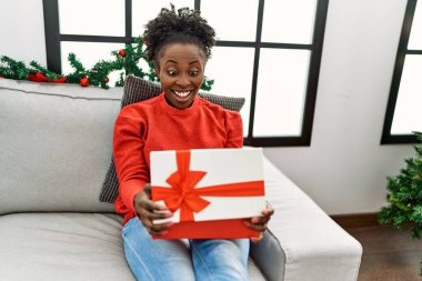 African american woman unpacking christmas gift sitting on sofa at home