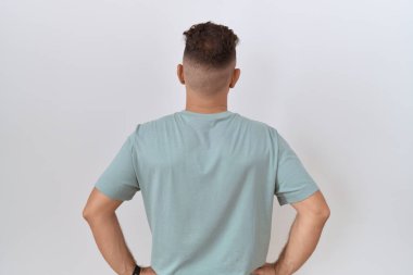 Hispanic man with beard standing over white background standing backwards looking away with arms on body 