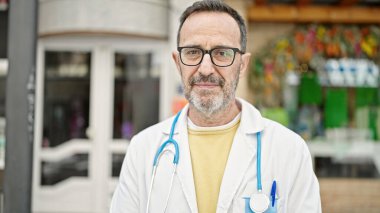 Sokakta ciddi bir ifadeyle duran orta yaşlı bir doktor.