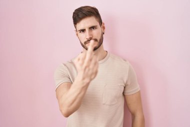 Hispanic man with beard standing over pink background showing middle finger, impolite and rude fuck off expression 