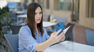 Kahve dükkanının terasında akıllı telefon kullanan genç ve güzel bir İspanyol kadın.