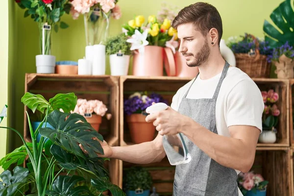 Young caucasian man florist using diffuser watering plant at flower shop
