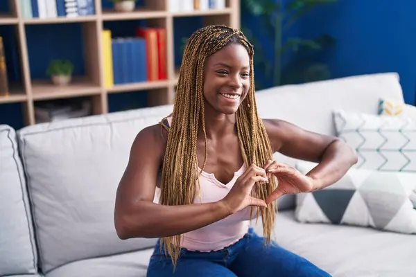 African american woman doing heart gesture with hands sitting on sofa at home