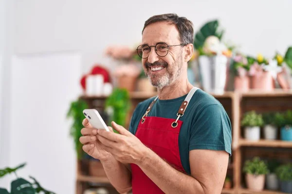 中年男人花匠用智能手机对花店充满自信地微笑 — 图库照片