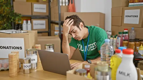 Young hispanic man volunteer using laptop stressed at charity center