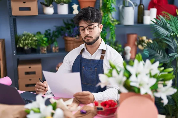 Young hispanic man florist reading document at florist shop