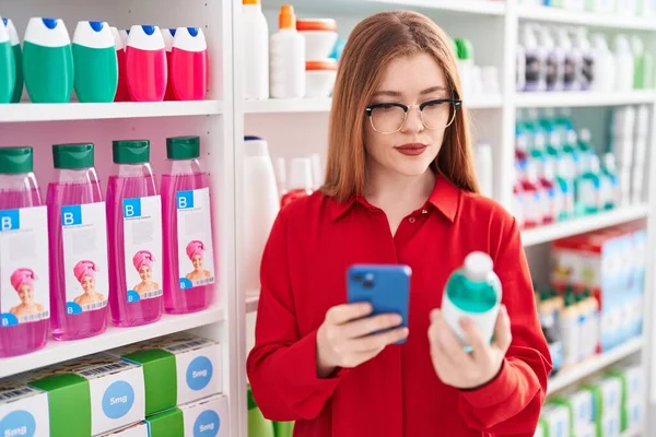 在药店用智能手机装药瓶的红头发年轻女性顾客 — 图库照片