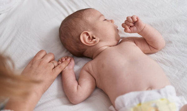 Adorable caucasian baby lying on bed holding mother finger at bedroom