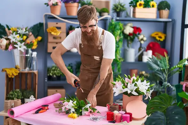 Young redhead man florist make bouquet of flowers at flower shop