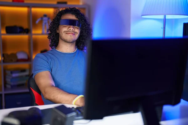 Young latin man streamer playing video game using virtual reality glasses at gaming room
