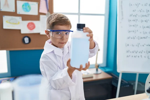 在实验室教室里 他那可敬的惊慌失措的男孩微笑着 自信地拿着装有液体的瓶子 — 图库照片
