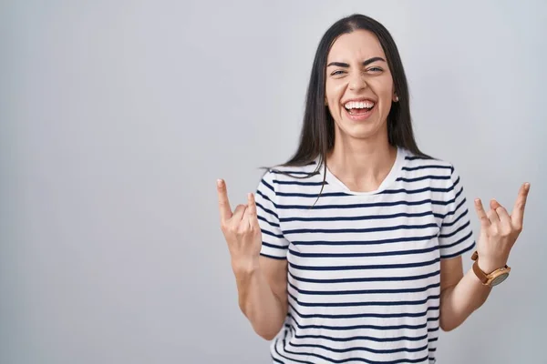 若いブルネットの女性は 手を挙げてロックシンボルを行うクレイジーな表情で叫ぶストライプTシャツを着ています ミュージックスター ヘビーミュージックコンセプト — ストック写真