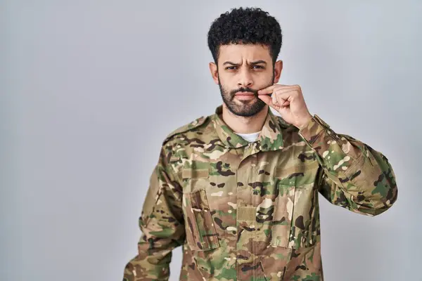 Arab man wearing camouflage army uniform mouth and lips shut as zip with fingers. secret and silent, taboo talking