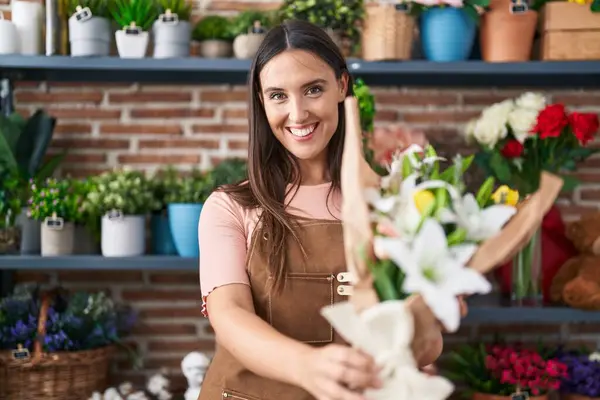 Young beautiful hispanic woman florist holding bouquet of flowers at flower shop