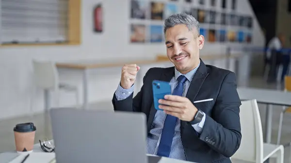 若いヒスパニック男性ビジネスワーカーは オフィスで優勝したジェスチャーでスマートフォンを見ています — ストック写真