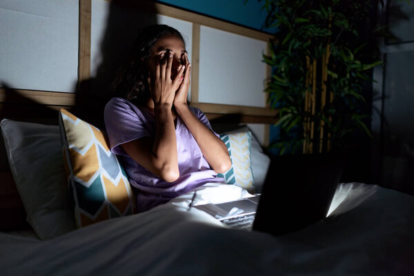 Молодая африканская американка с ноутбуком сидит на кровати в спальне