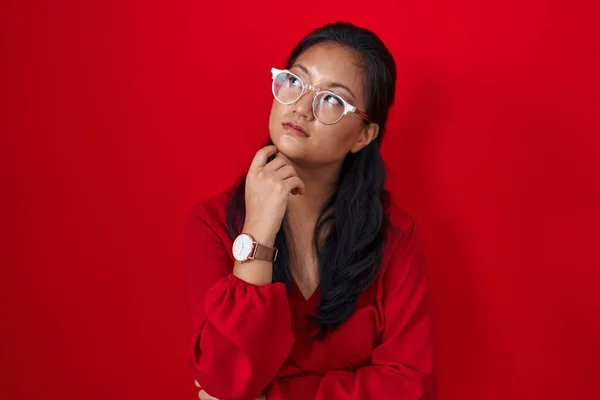 Asyalı Genç Bir Kadın Kırmızı Arka Planda Duruyor Elleri Çenesinde — Stok fotoğraf
