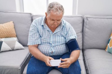 Orta yaşlı, kır saçlı, nabız ölçer kullanan bir adam.