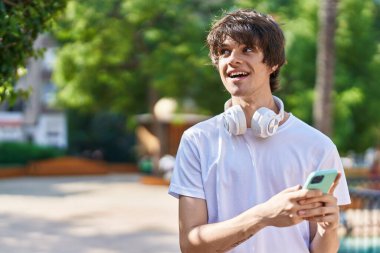 Young blond man smiling confident using smartphone at park